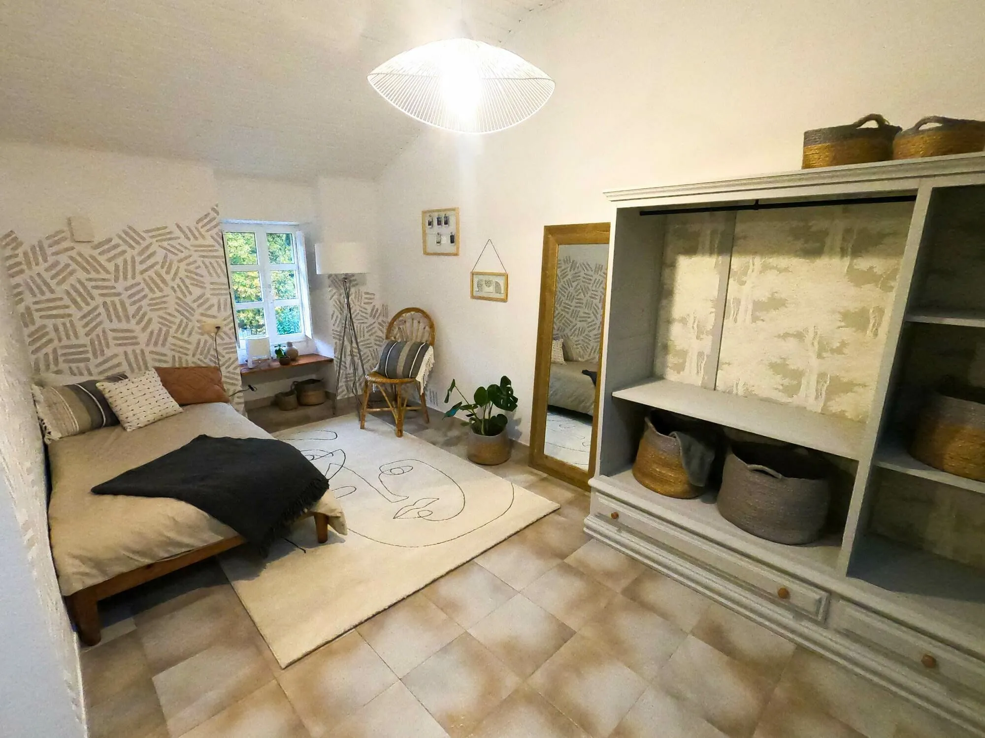 A habitación 104 despois do seu redeseño: unha cama dobre contra unha parede pintada a man, un espello de corpo enteiro, cestos de fibra e unha planta