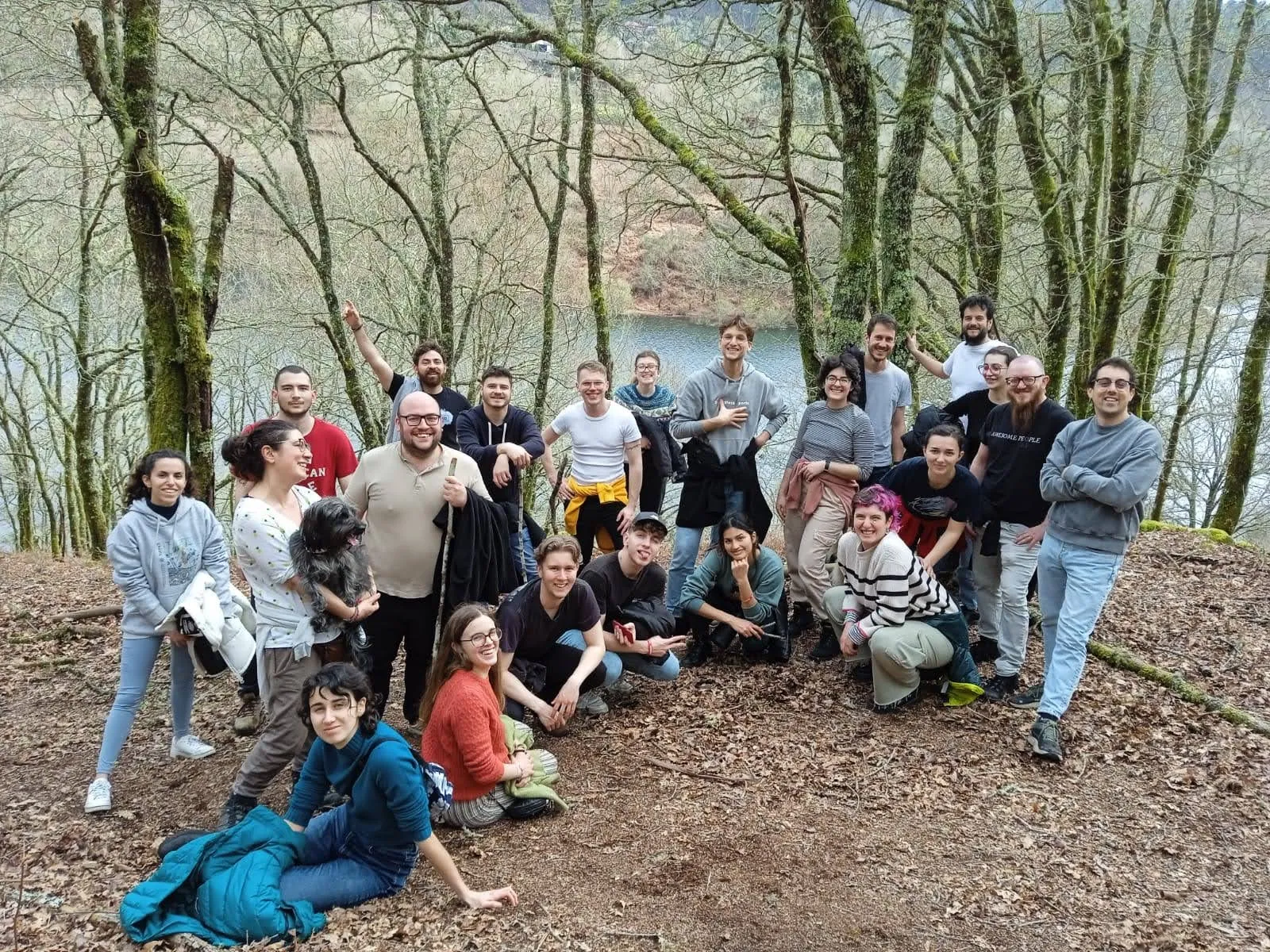 Un grupo de unas treinta personas posando en una ladera cubierta de hojas sobre un embalse, entre árboles sin hojas