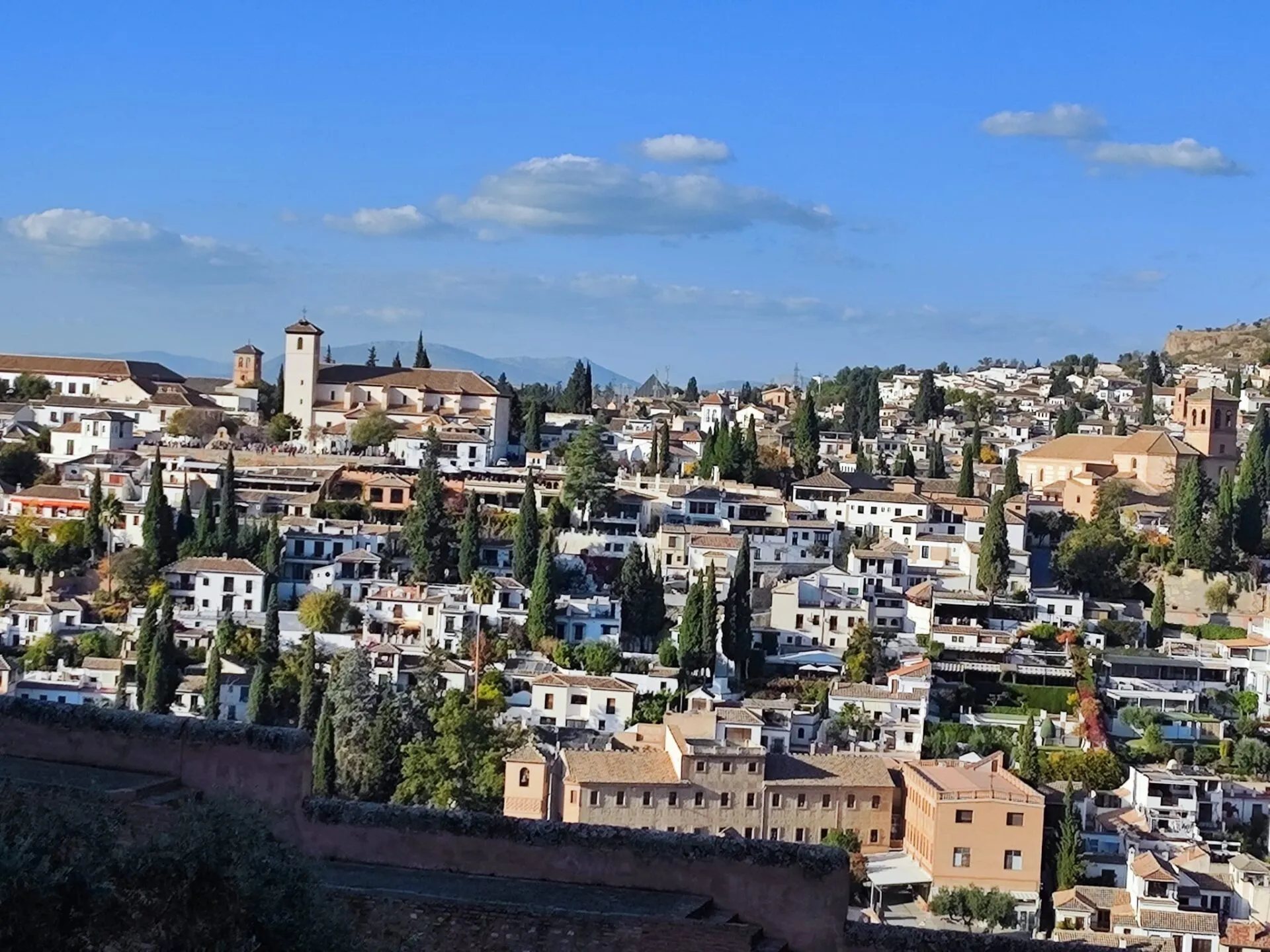Vista sobre una ladera de casas encaladas, cipreses y una torre de iglesia en el Albaicín de Granada