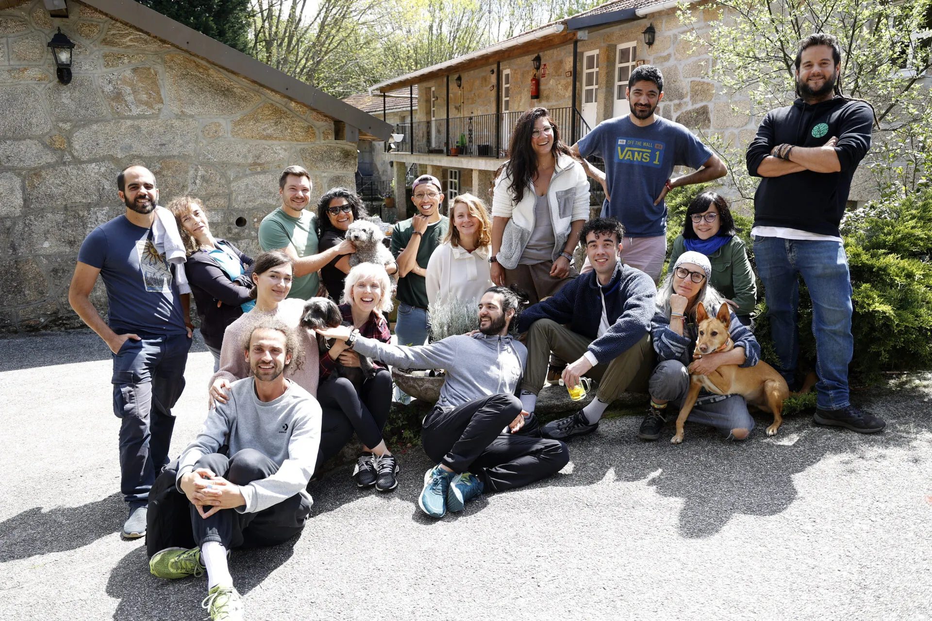 Un grupo dunhas dezaseis persoas posando nun patio de grava diante dunha casa de pedra, con dous cans entre elas
