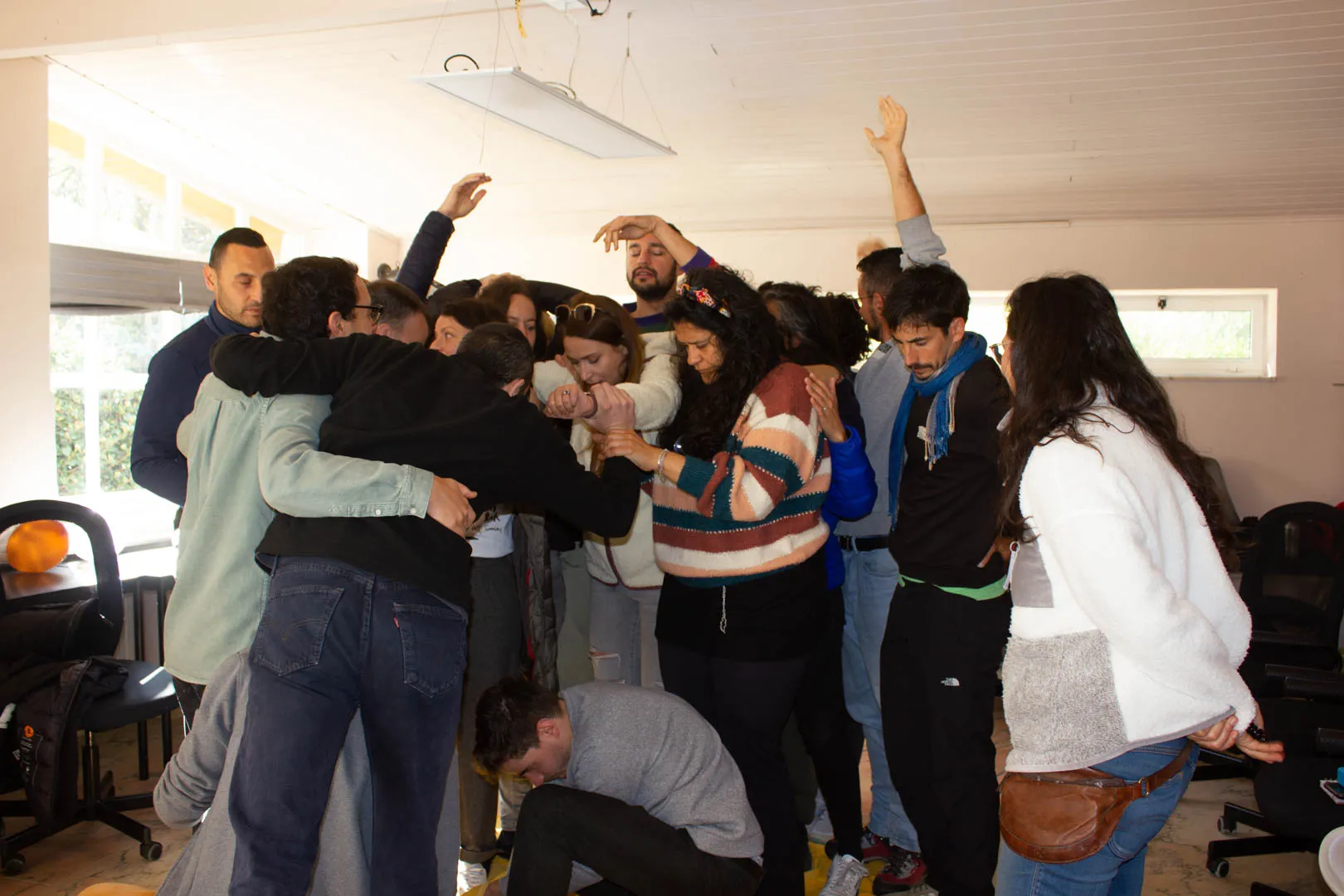 Grupo de un taller apiñado con los brazos entrelazados en una sala blanca y luminosa, con algunas manos levantadas