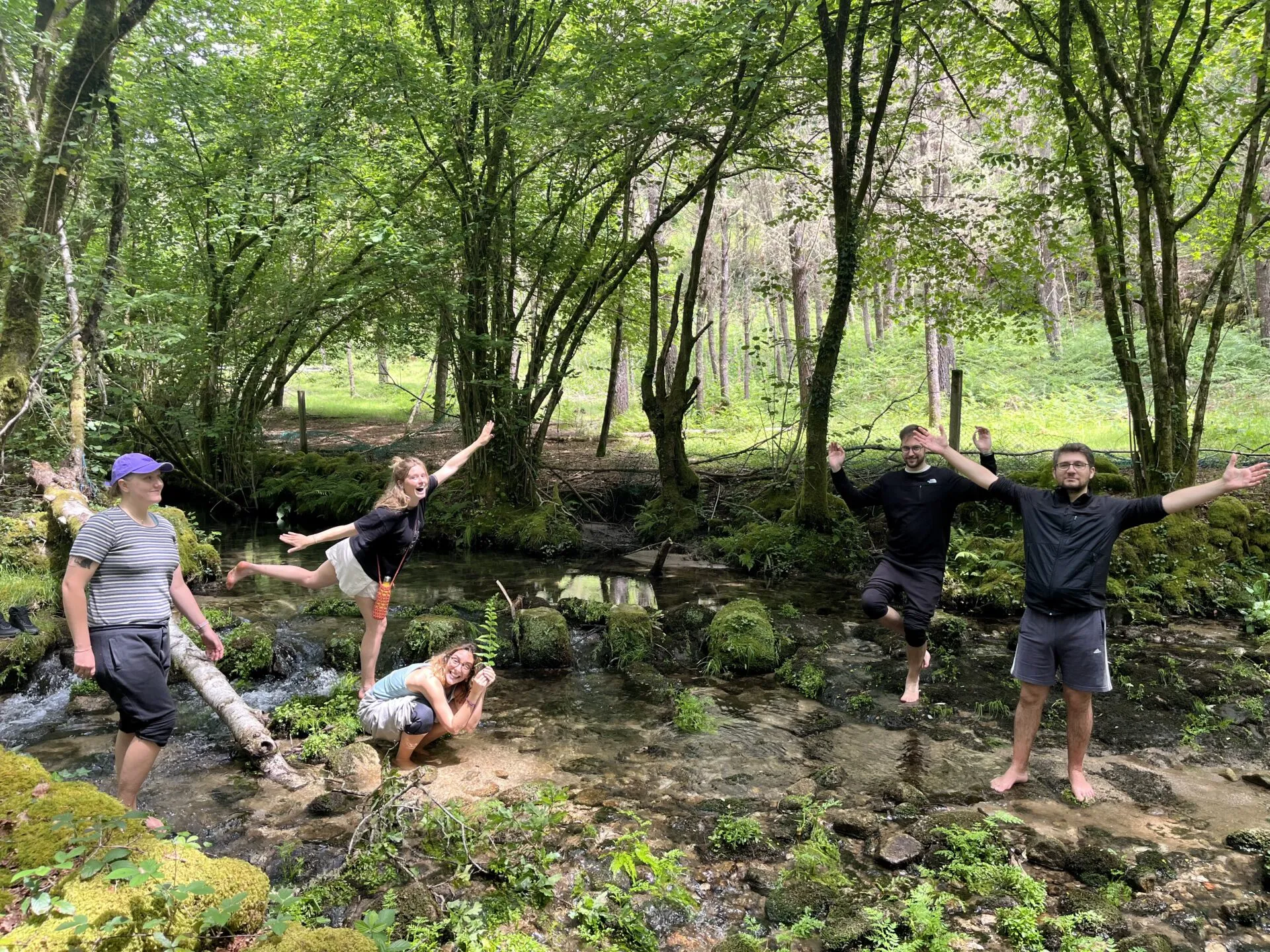 Cinco personas posando descalzas en un arroyo poco profundo que atraviesa un bosque verde cubierto de musgo