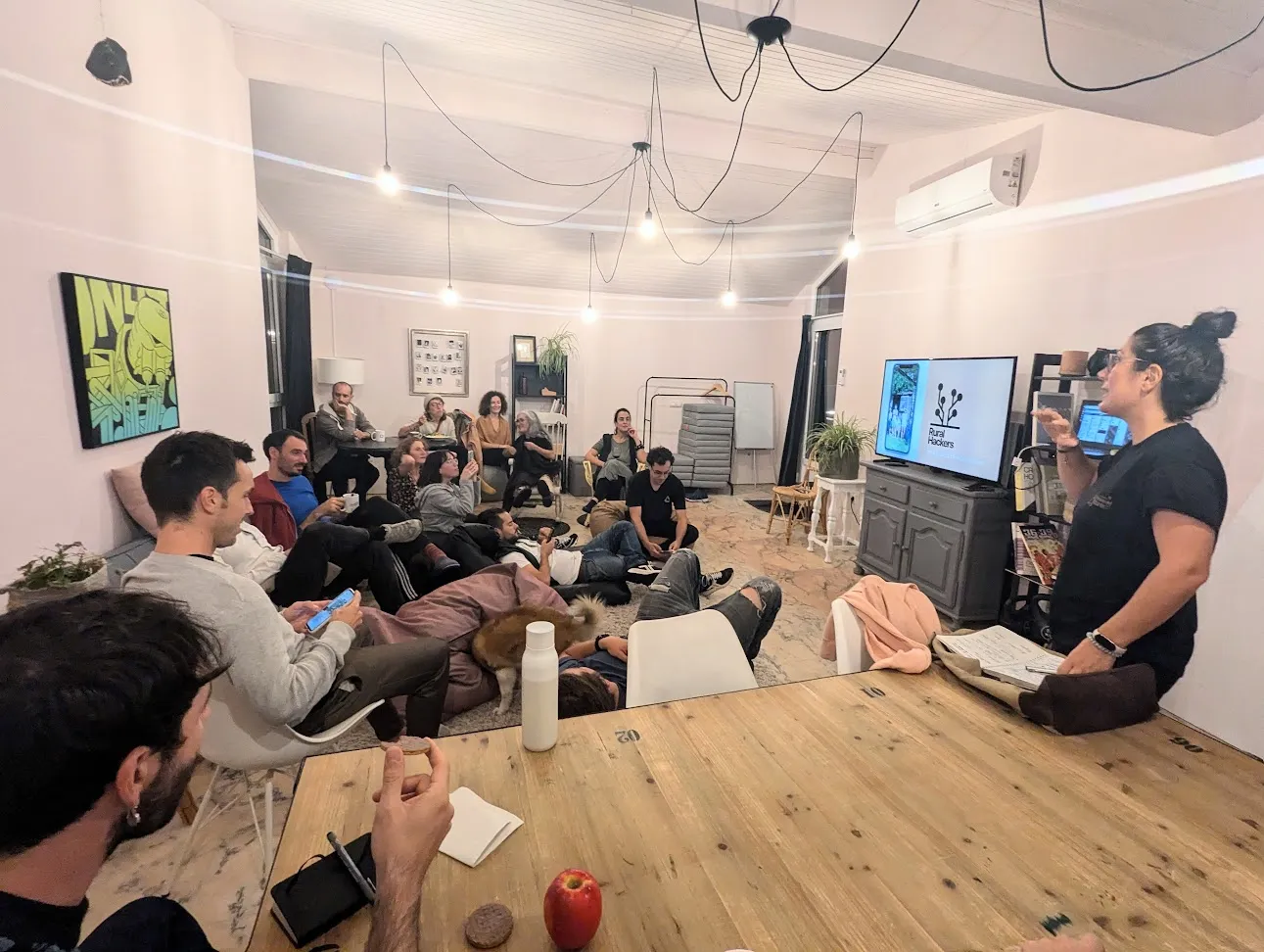 Unha muller presentando a carón dunha pantalla co logo de Rural Hackers, ante unha sala de xente sentada e deitada no chan