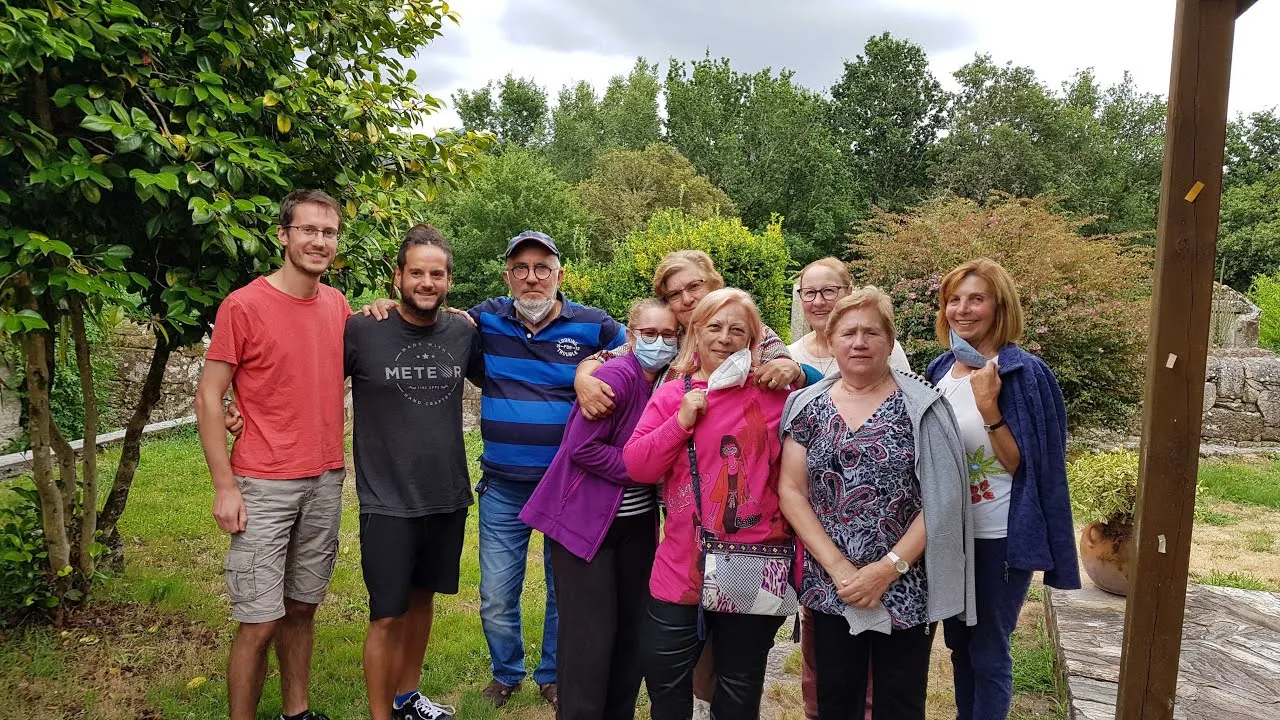 Dos jóvenes posando en un jardín con un grupo de mujeres mayores, algunas con mascarilla
