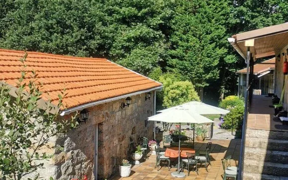 Edificio de pedra con tellado de tella laranxa xunto a unha terraza con parasol branco e cadeiras de xardín