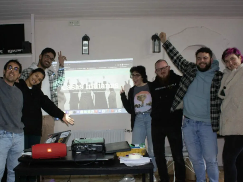 Oito persoas celebrando diante dunha web proxectada que di ‘Casas Indianas’, cun portátil e un proxector na mesa