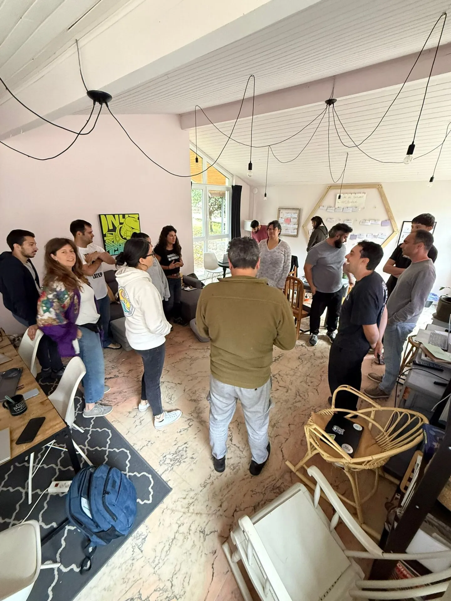 Unhas quince persoas de pé en círculo conversando na sala de coworking, con portátiles nunha mesa de madeira ao lado