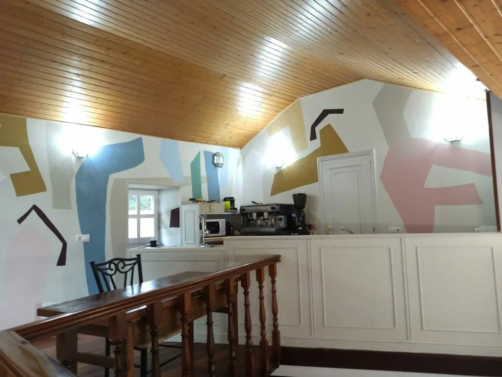 O café despois do seu redeseño: un mural abstracto en azul, ocre e rosa cubrindo as paredes, coa cafeteira debaixo
