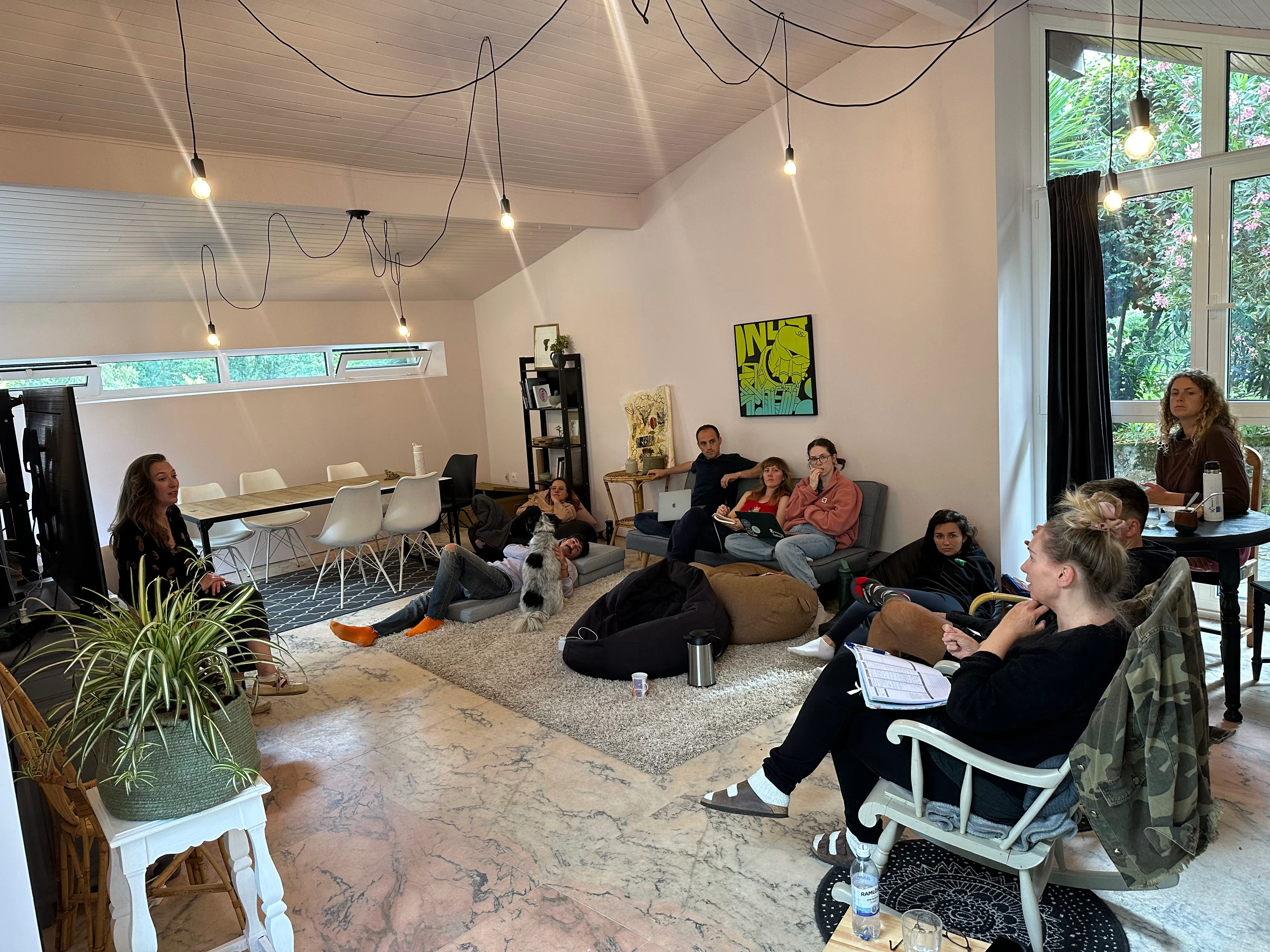 Gente reunida en el Chill Haus de Anceu, unos en el sofá, otros en el suelo con el perro, bajo las bombillas colgadas