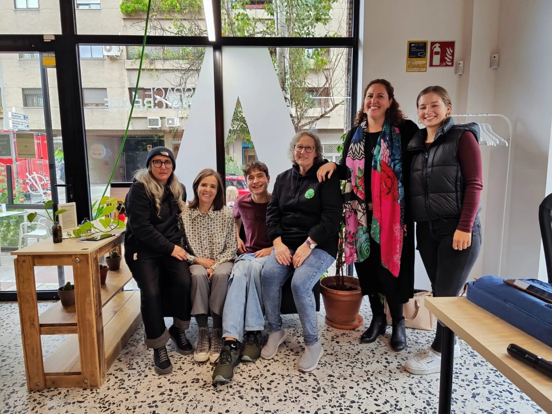 Seis personas posan juntas en una oficina luminosa a pie de calle, con un gran logotipo en el cristal y suelo de terrazo