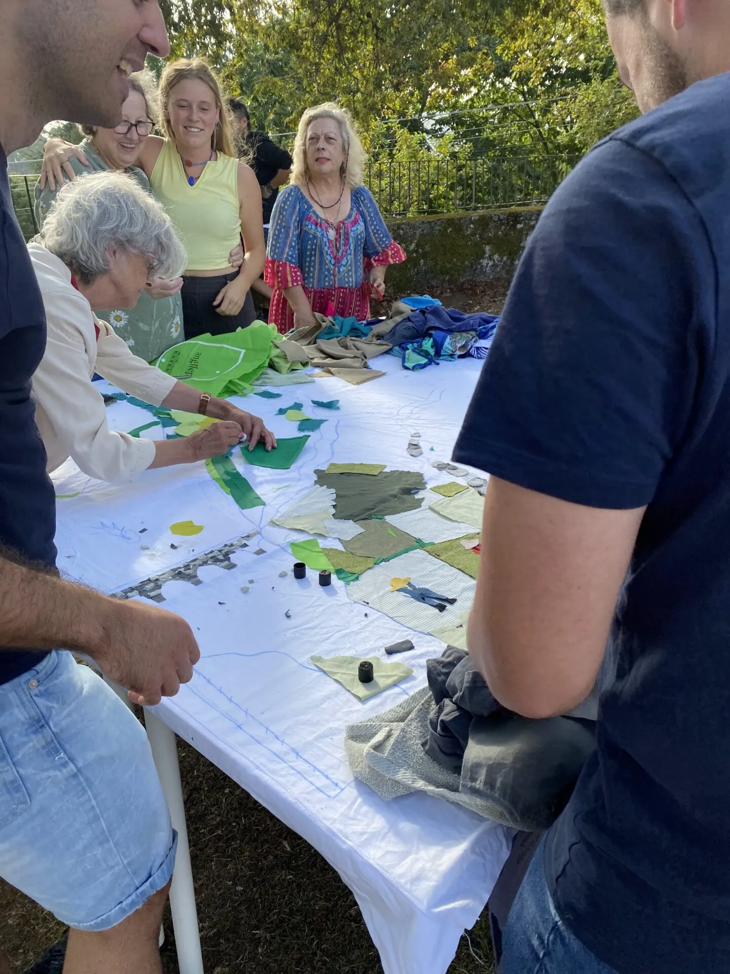 Varias persoas arredor dunha mesa ao aire libre compoñendo un mapa con retallos de tea verde sobre unha saba branca