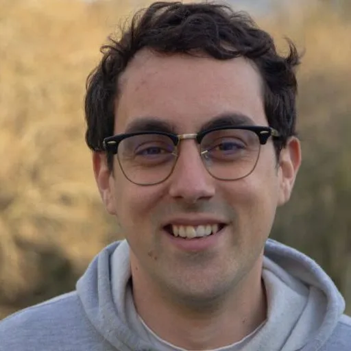 Nacho, sorrindo, con sudadeira gris e lentes redondas
