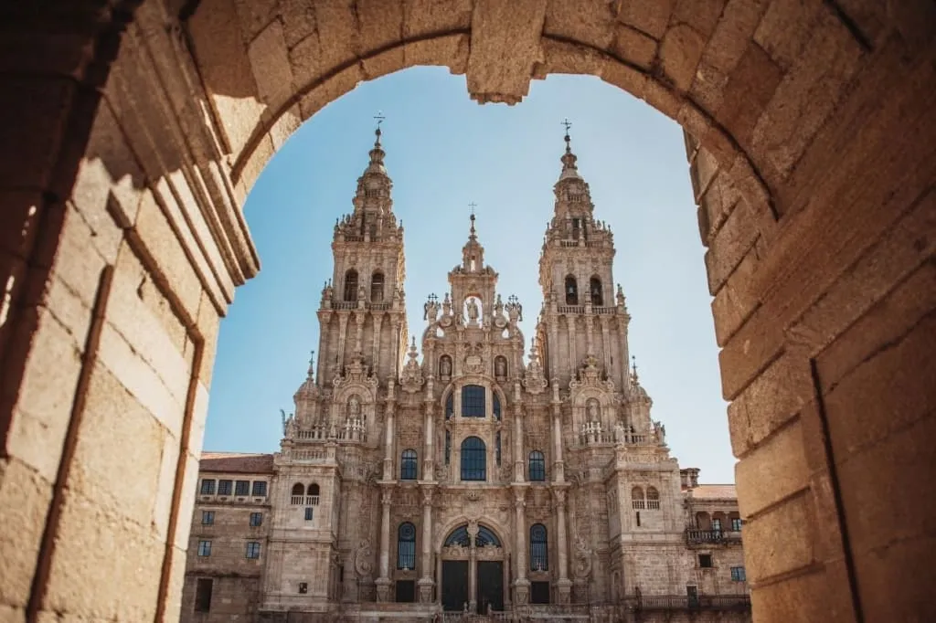 Fachada barroca da catedral de Santiago de Compostela enmarcada por un arco de pedra baixo un ceo despexado