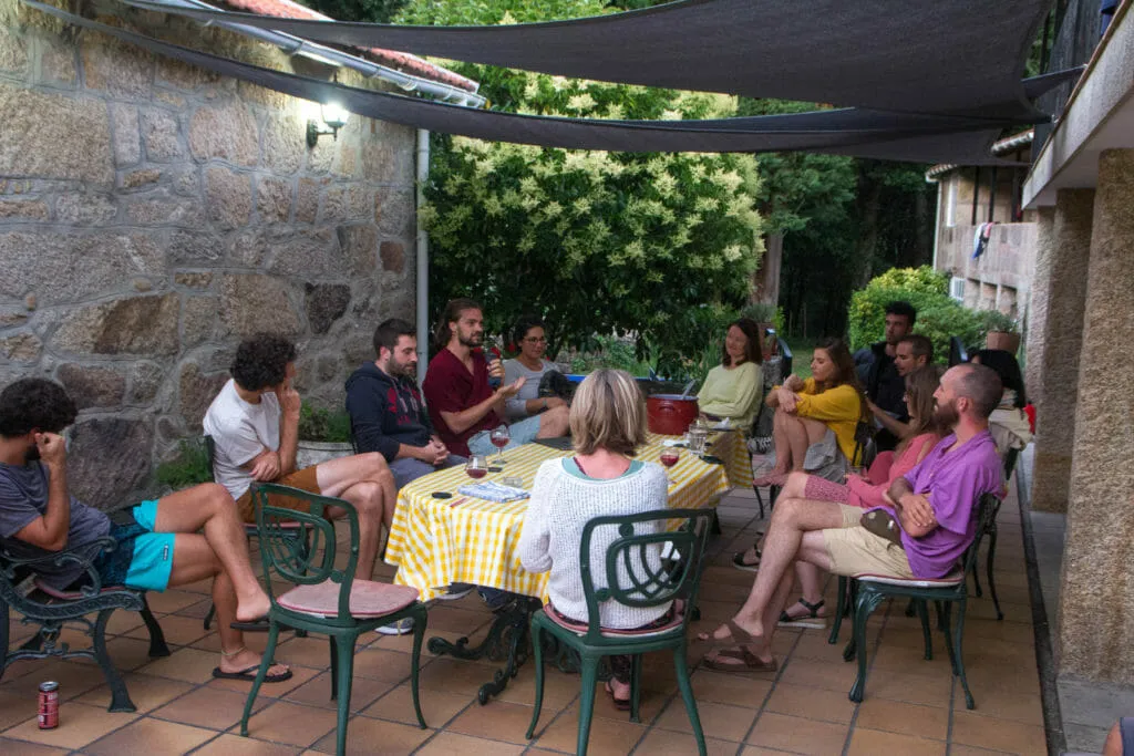 Amigos conversando arredor dunha mesa con mantel amarelo de cadros nunha terraza de pedra á sombra