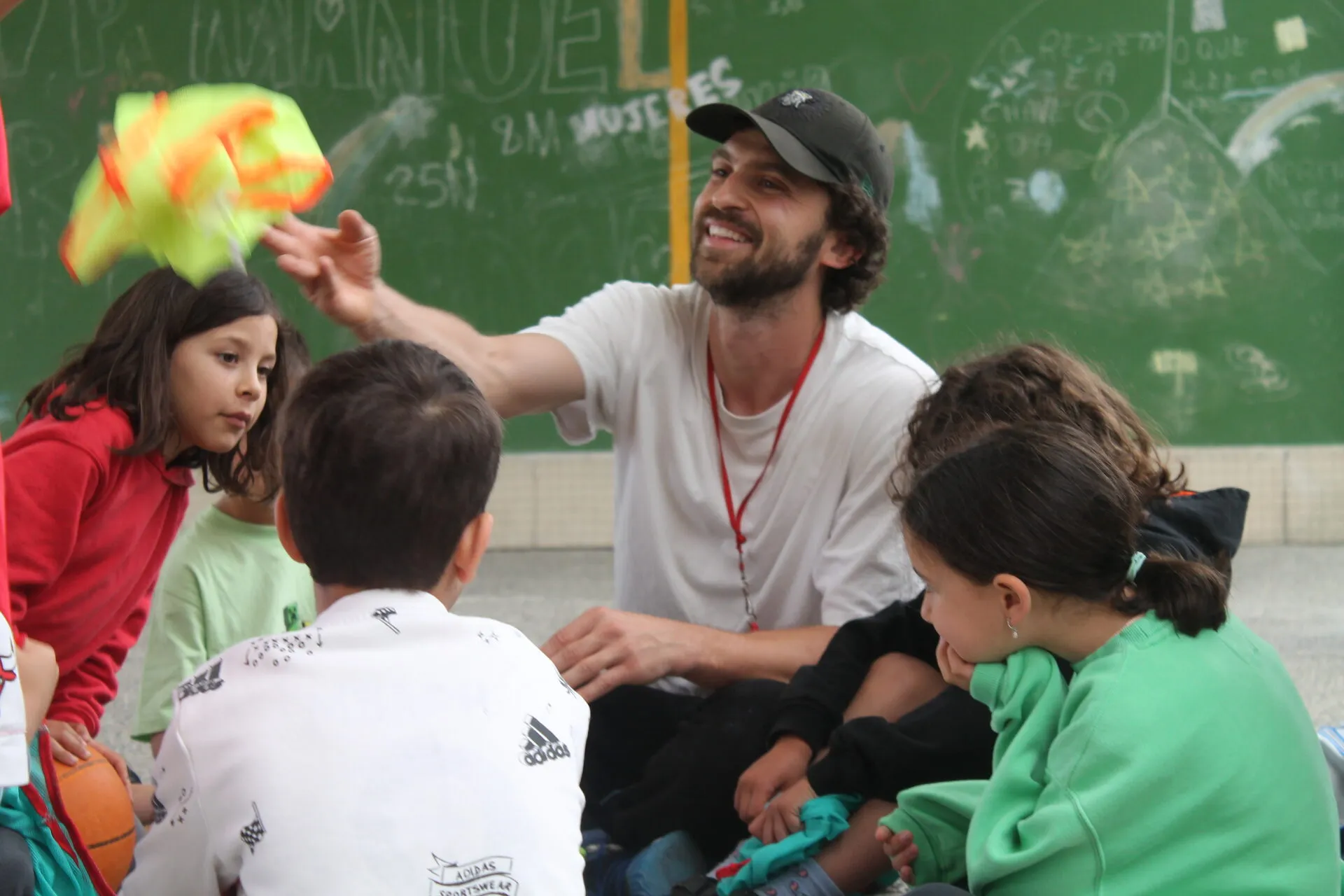 Víctor sentado en el suelo de un patio de colegio con un grupo de niños alrededor, sujetando un manojo de petos de colores