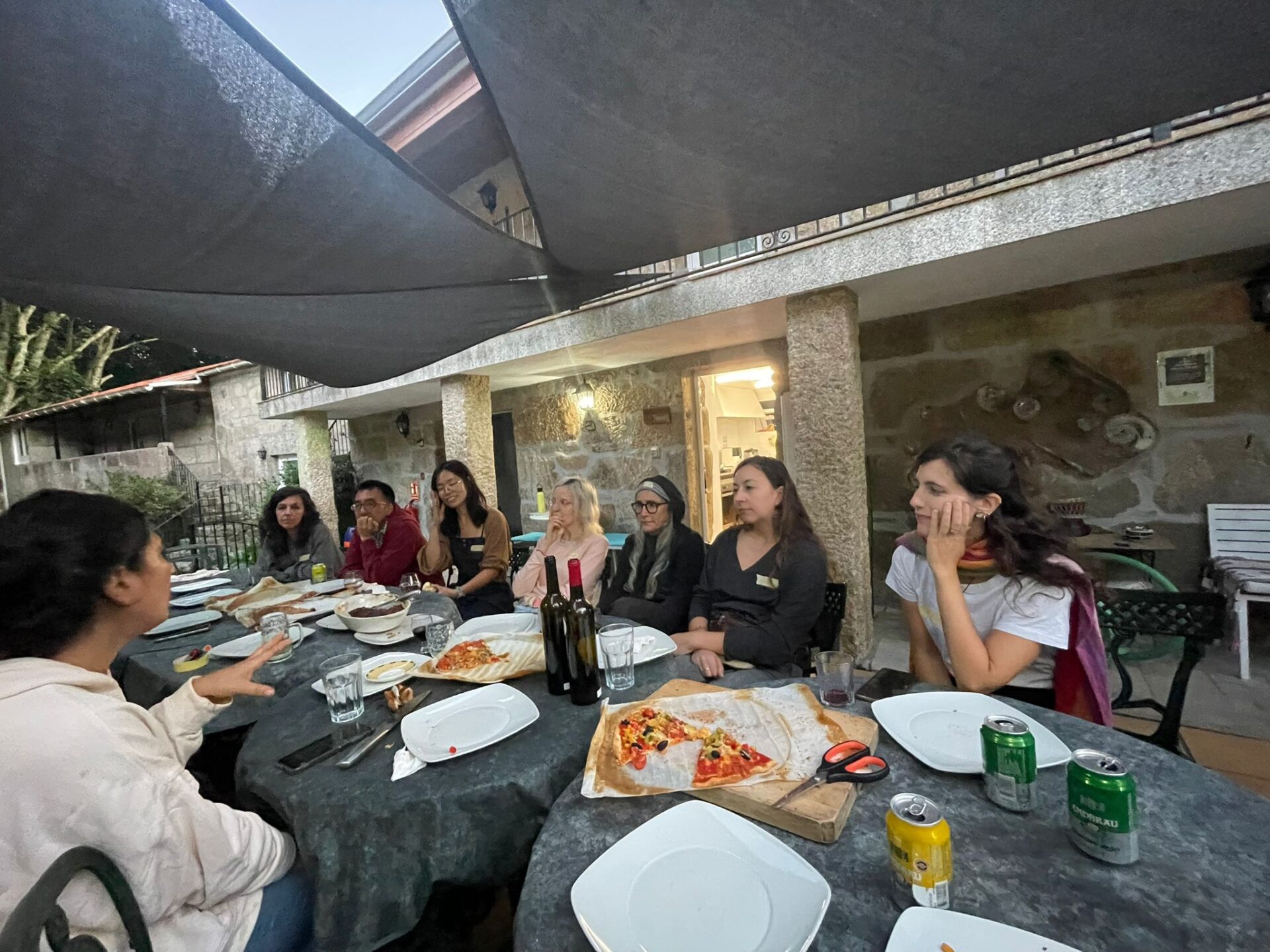 Sharing a meal is where community begins."
Alt text: "Group of people sitting around a table sharing pizza and wine at a community dinner at Anceu Coliving