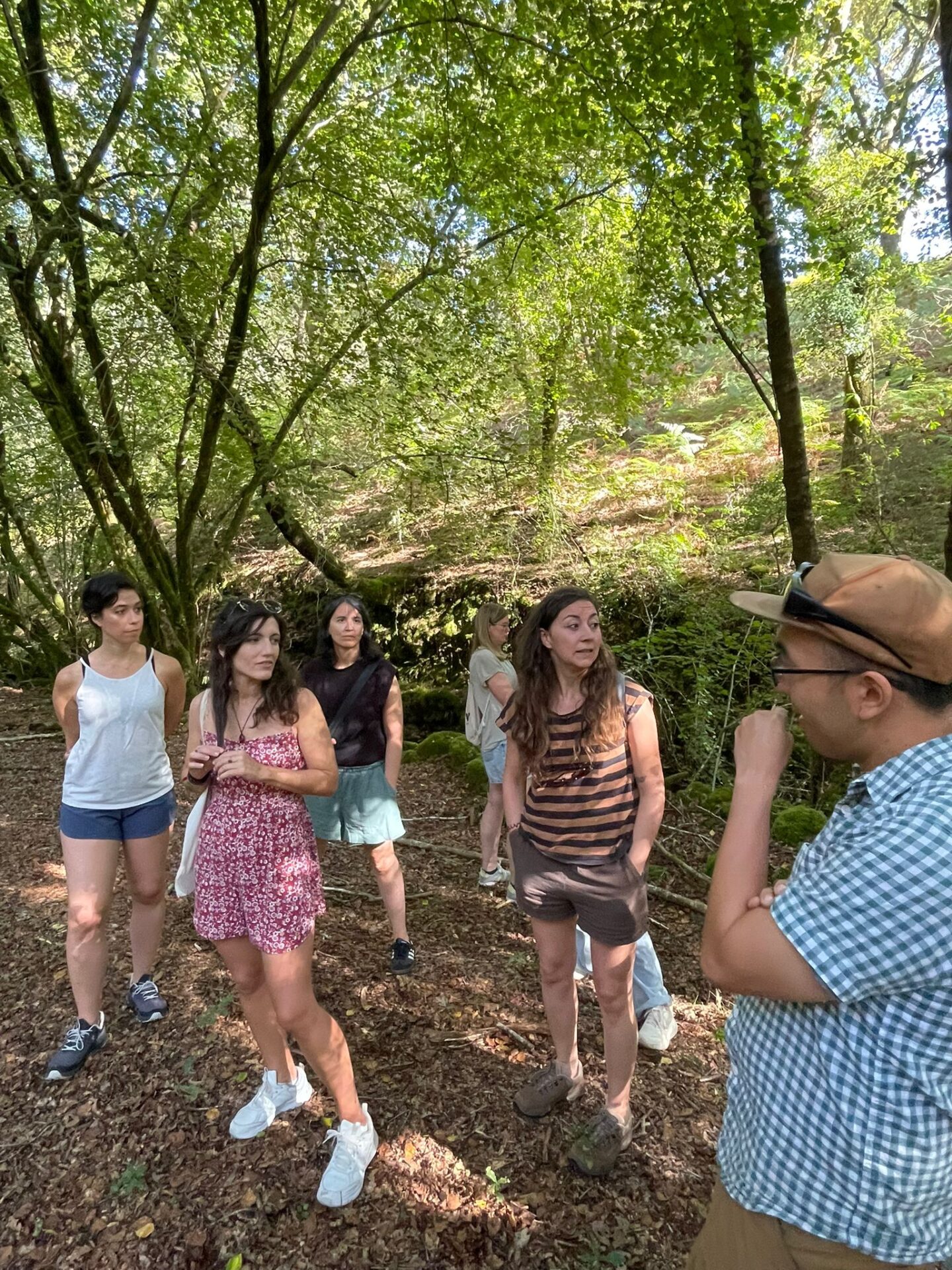 A group of people walking through a green forest path in rural Galicia during a community outing