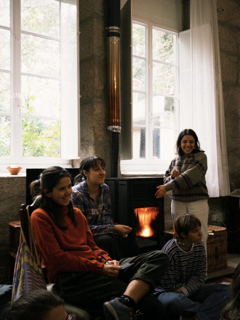 Two women and a child sitting together by a lit fireplace inside Anceu Coliving during the winter season